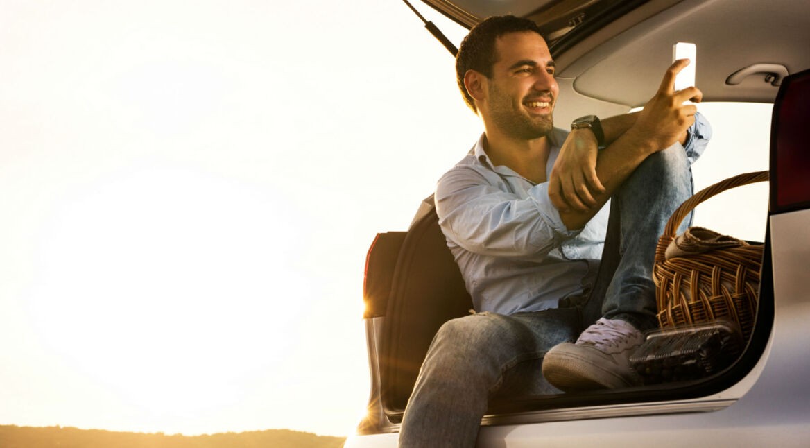 Mann sitzt im Kofferraum mit dem Smartphone.