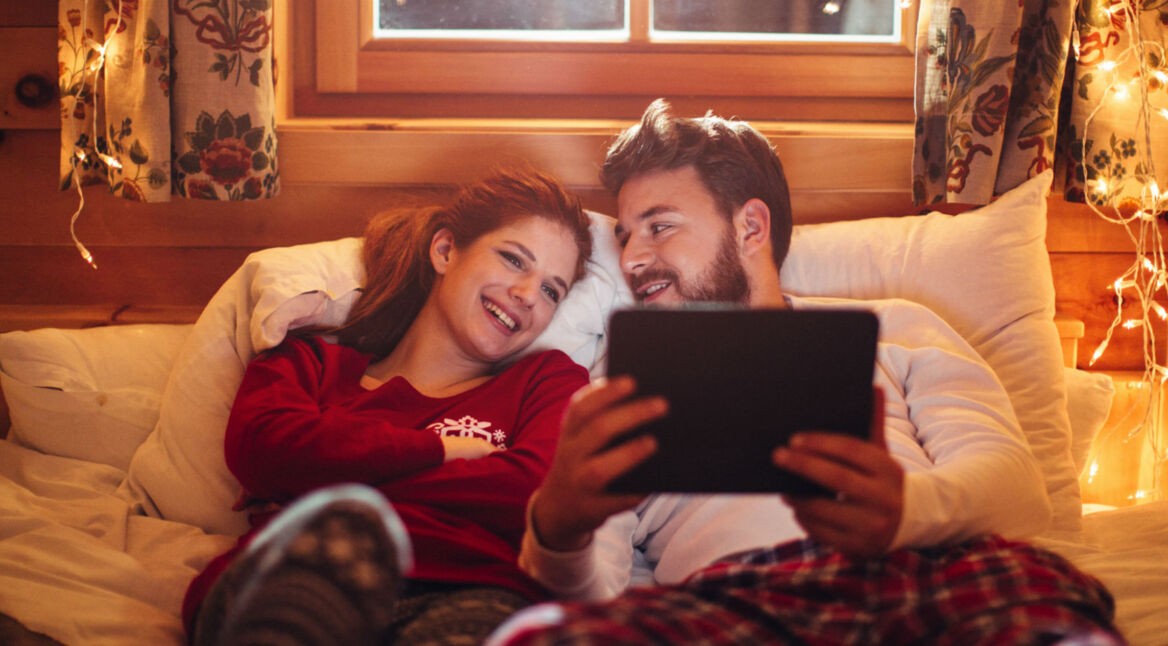 Pärchen liegt im Bett und schaut Filme auf dem Tablet.