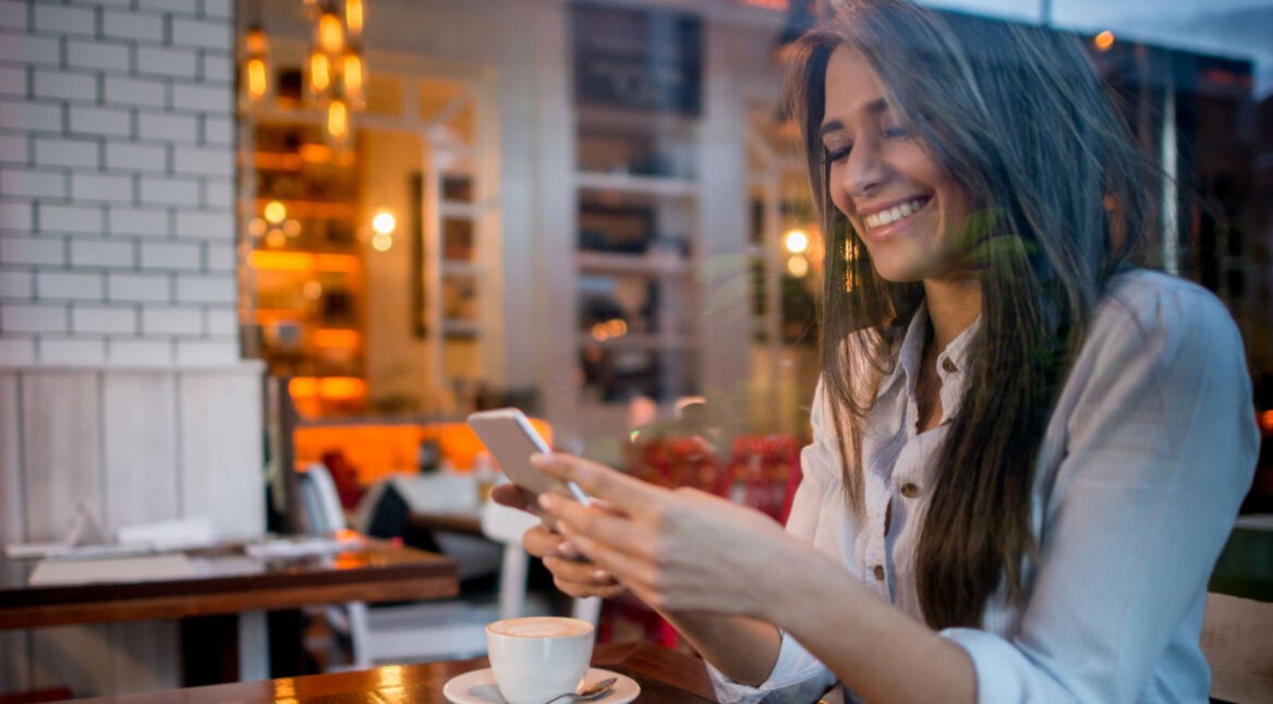 Frau trinkt Kaffee und schaut auf ihr Smartphone.