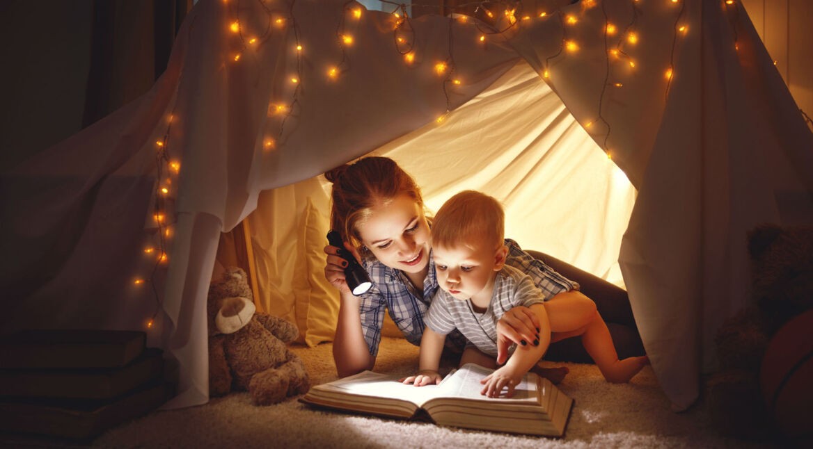 Junge Frau leuchtet mit Taschenlampe auf ein Buch, plus Baby.