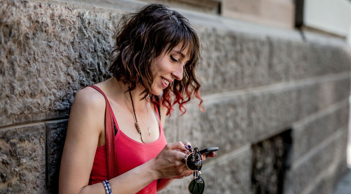 Frau in rotem Top schaut auf ihr Smartphone.