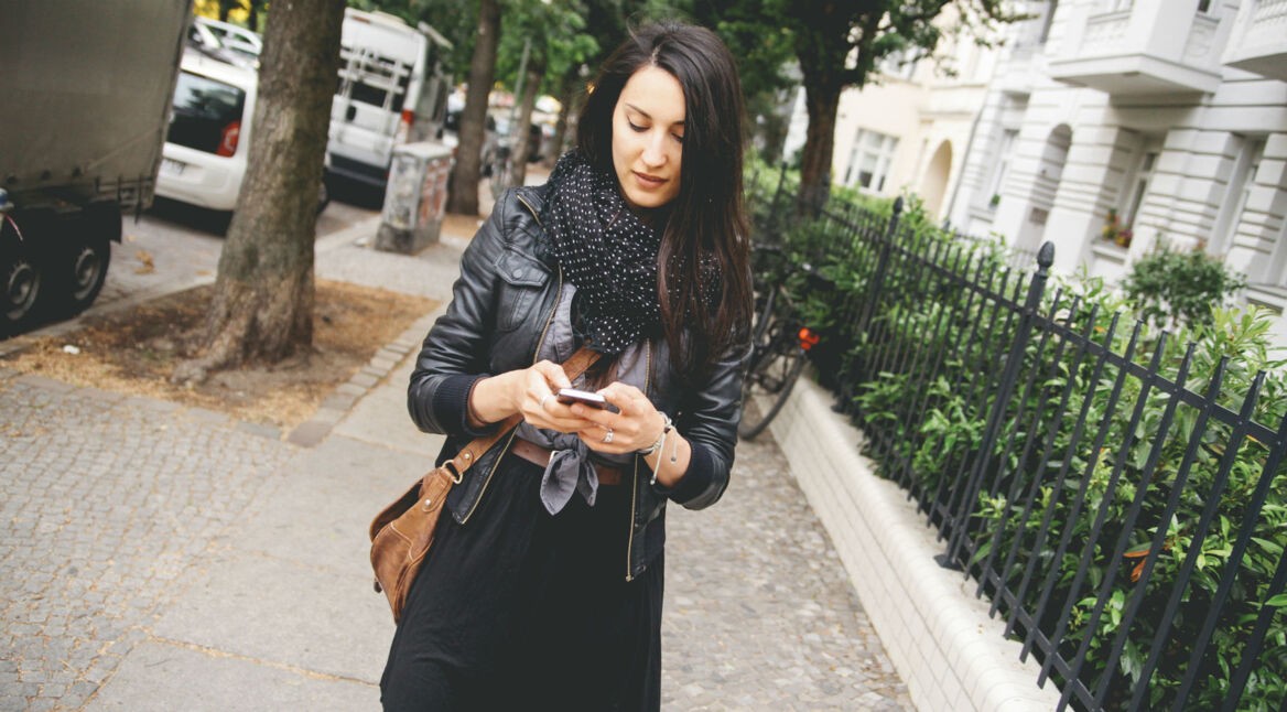 Frau spaziert und schaut dabei auf ihr Smartphone.