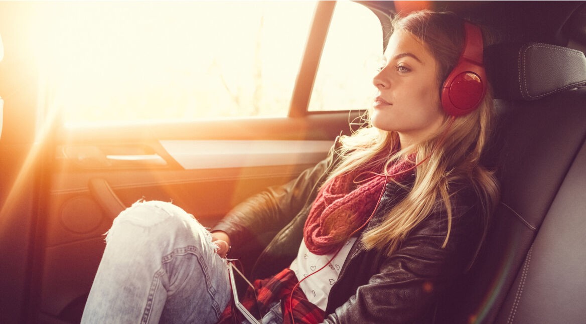 Frau geniesst Hörspiele im Auto mit Kopfhörer