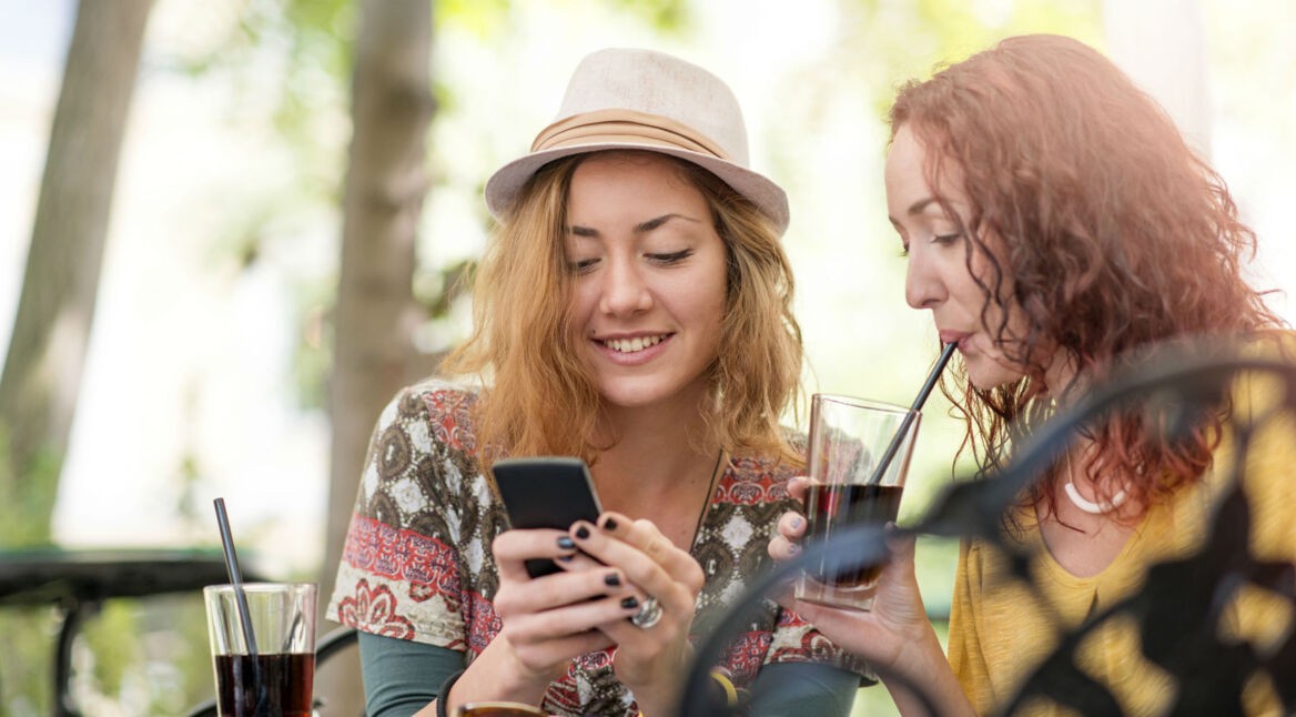 Junge Frau zeigt ihrer Freundin etwas auf ihrem Smartphone.