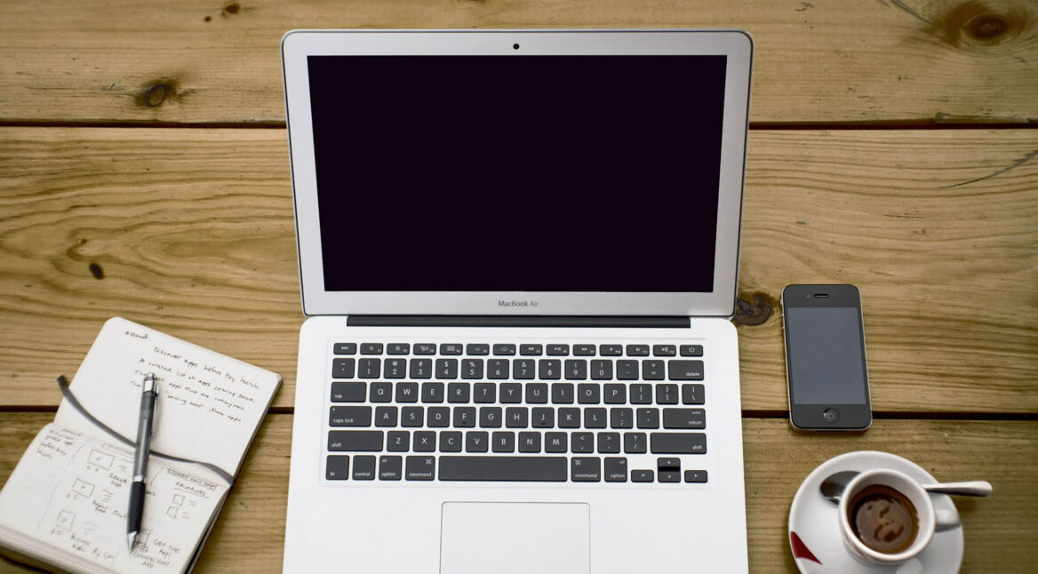 iPhone und Notebook liegen neben Espressotasse auf einem Holztisch.