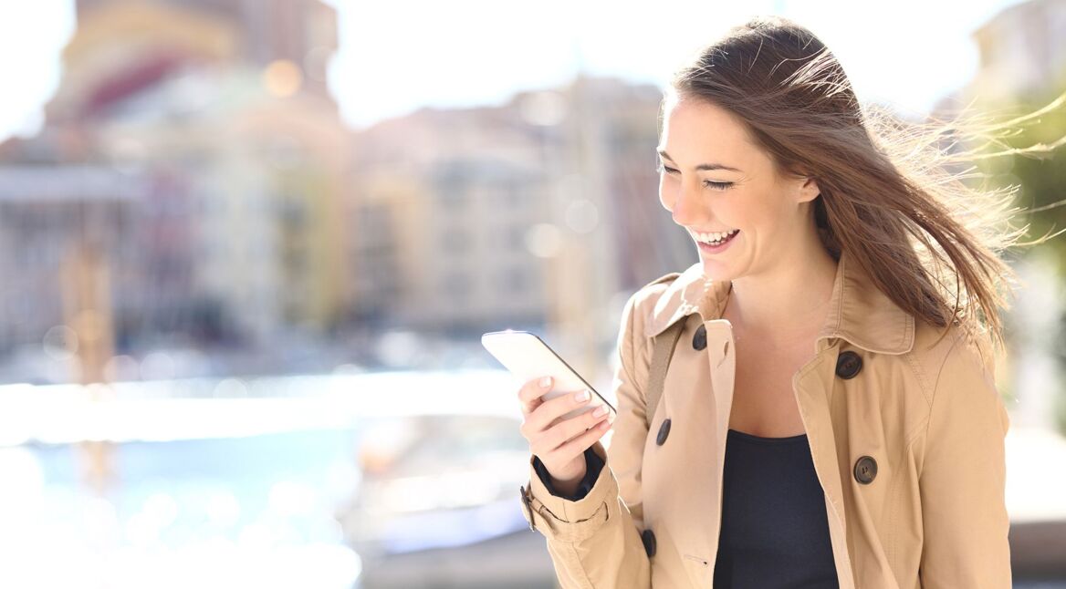 Lachende Frau mit Smartphone draußen.