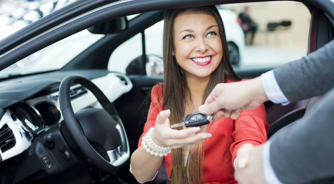 Junge Frau kauft ein neues Auto und bekommt die Schlüssel überreicht.