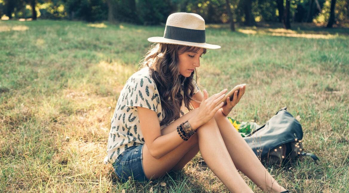 Junge Frau sitzt draußen im Park und schaut auf ihr Smartphone.
