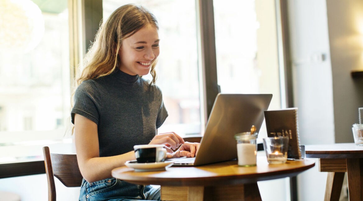 Junge Frau lächelt und surft am Laptop.