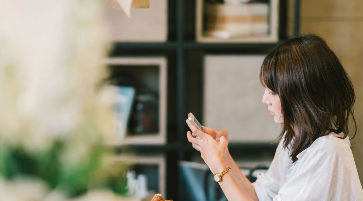 Junge Frau sitzt im Cafe und schaut auf ihr Smartphone.