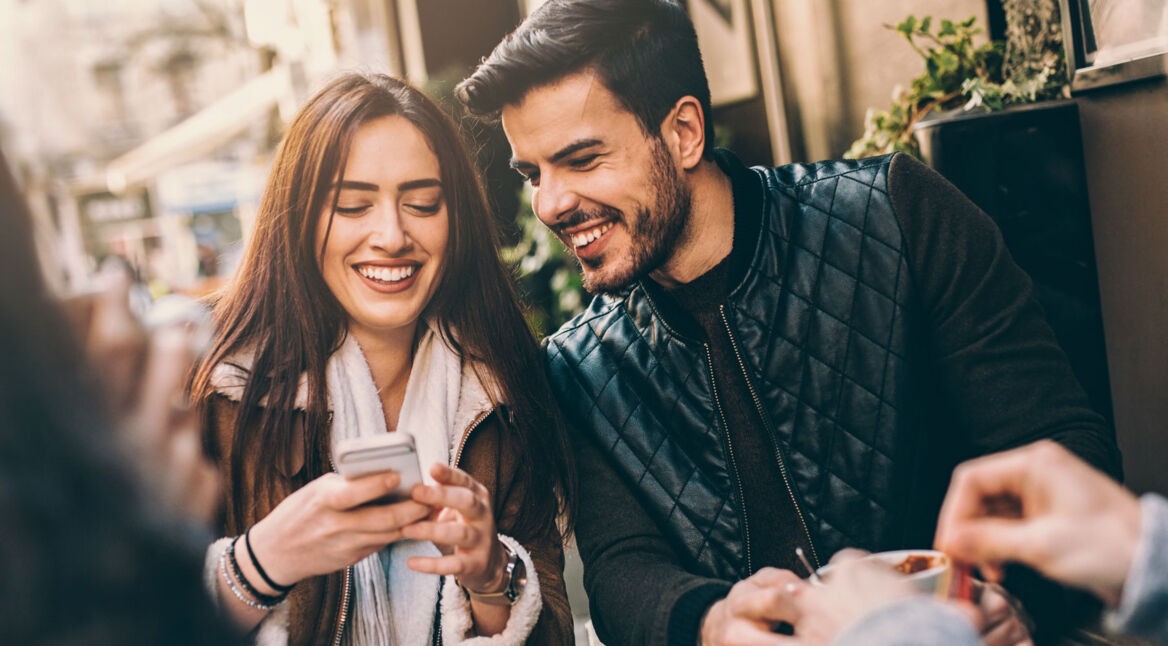 Pärchen sitzt im Restaurant und schaut zusammen auf ein Smartphone.