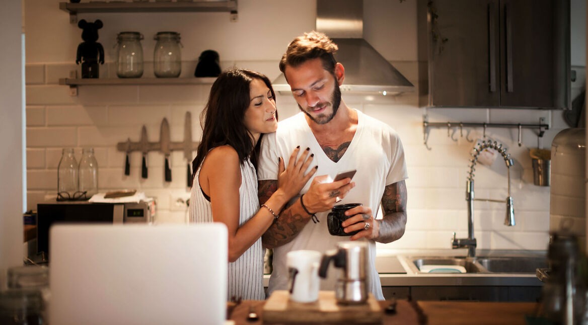 Pärchen steht in der Küche mit dem Smartphone.