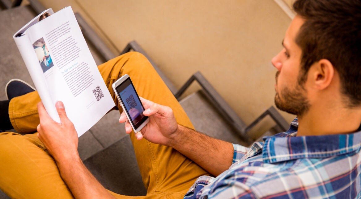 Ein Mann scannt einen QR-Code aus einer Zeitung ab.
