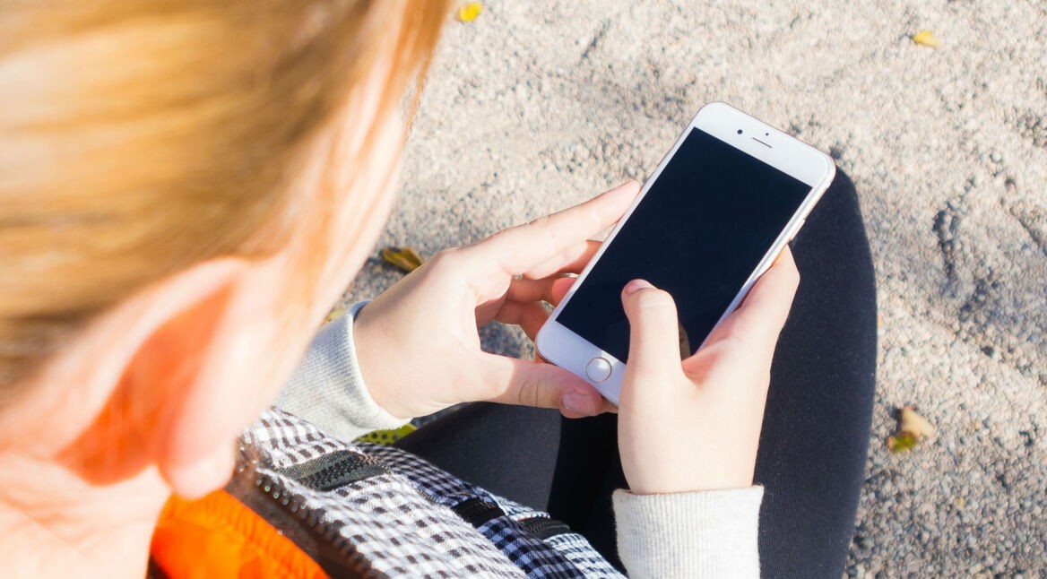 Mädchen mit blonden Haaren schaut auf ihr iPhone.