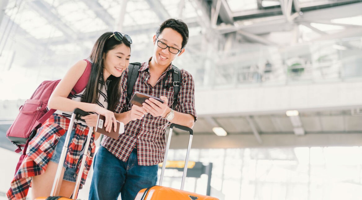 Junges asiatisches Paar mit Smartphone am Flughafen.