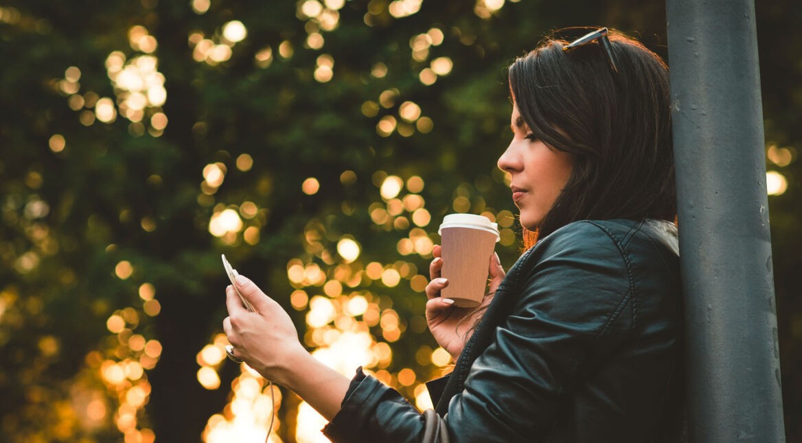 Junge Frau checkt draußen Mails an ihrem Smartphone.