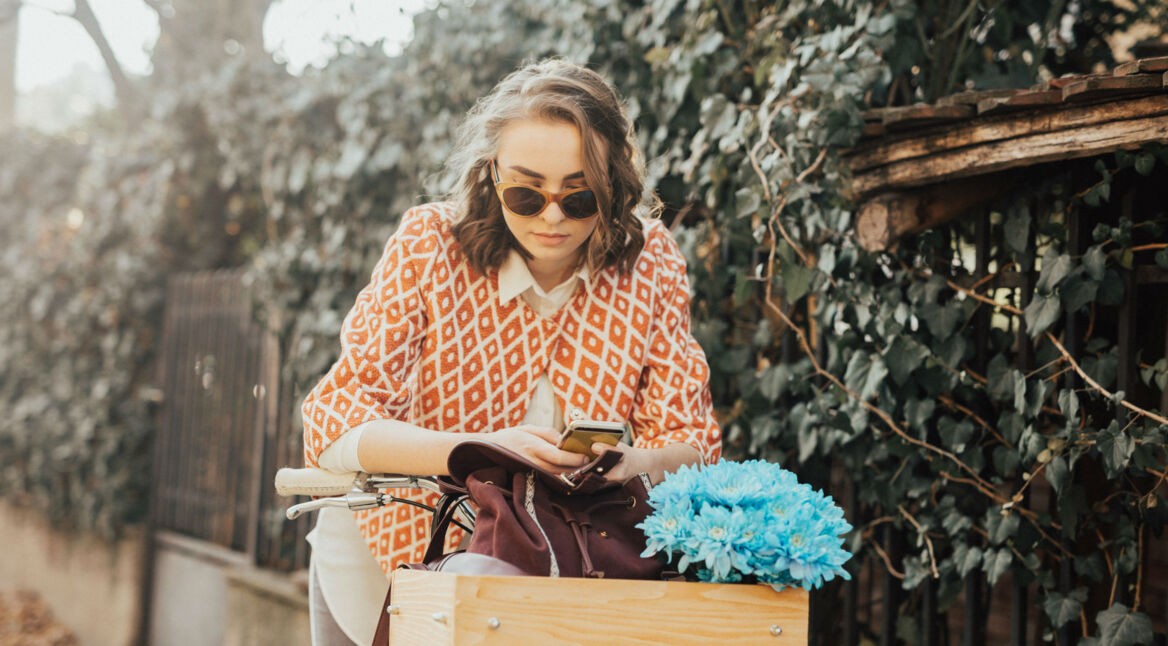 Junge Frau sitzt auf dem Fahrrad und tippt eine Nachricht auf ihrem Smartphone.