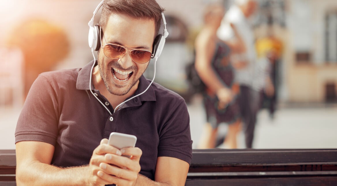 Mann mit Kopfhörern spielt am iPhone.