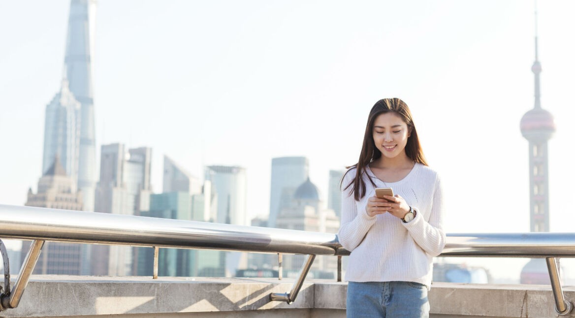 Junge Asiatin ist unterwegs und schaut auf ihr Smartphone