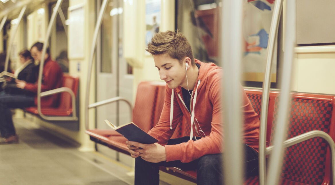 Junger Mann hört auf seinem Smartphone Musik und liest nebenbei ein Buch.