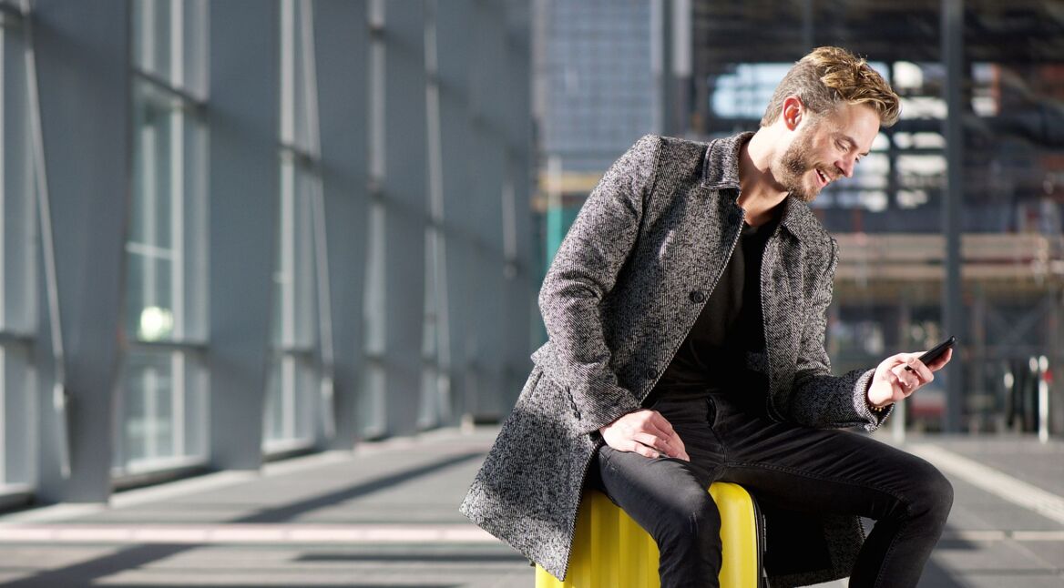 Lachender Mann mit Smartphone am Flughafen