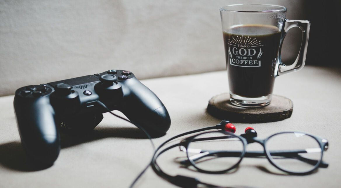 Schwarzer PS4-Controller liegt neben Brille und Kaffee auf einem Schreibtisch.