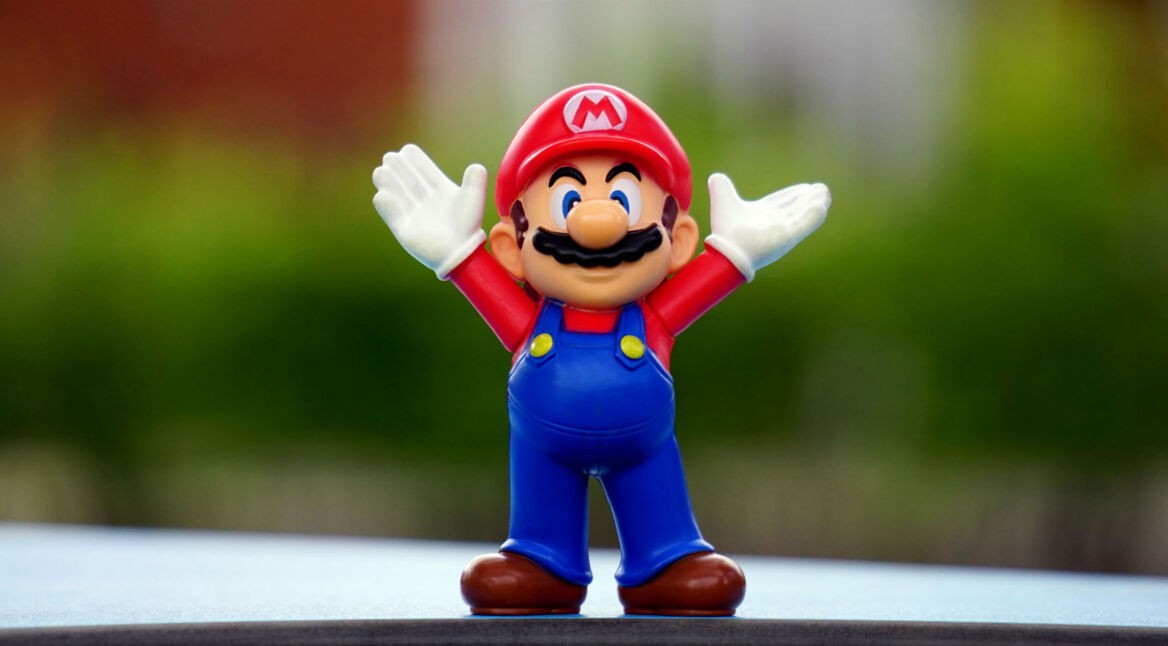 Super Mario-Figur steht auf Tisch und streckt die Arme in die Höhe.