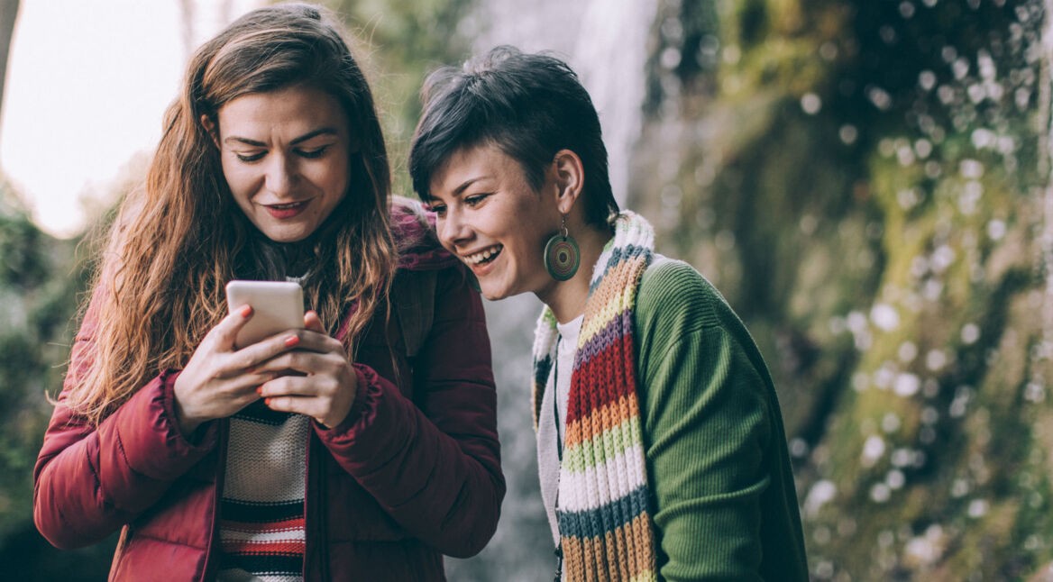 Zwei Freundinnen schauen lachend auf ein Smartphone.