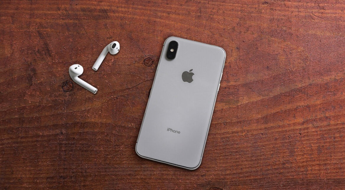 iPhone X und AirPods liegen auf hölzernem Tisch.