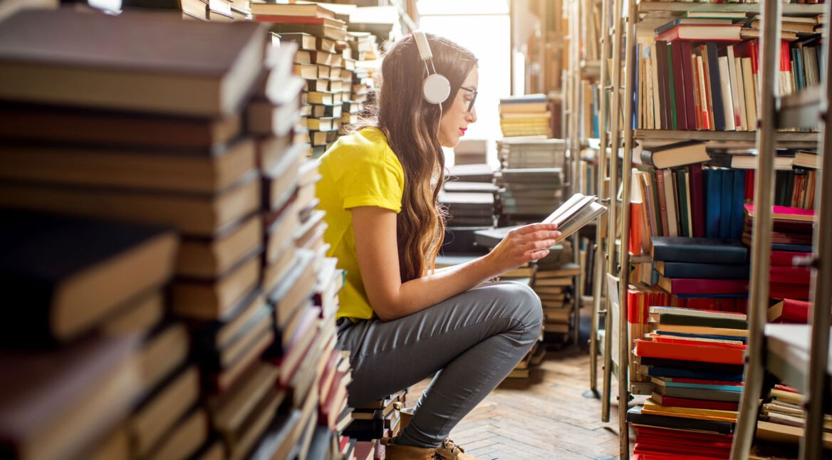 Junge Frau liest ein Buch, während sie über Kopfhörer Musik hört.