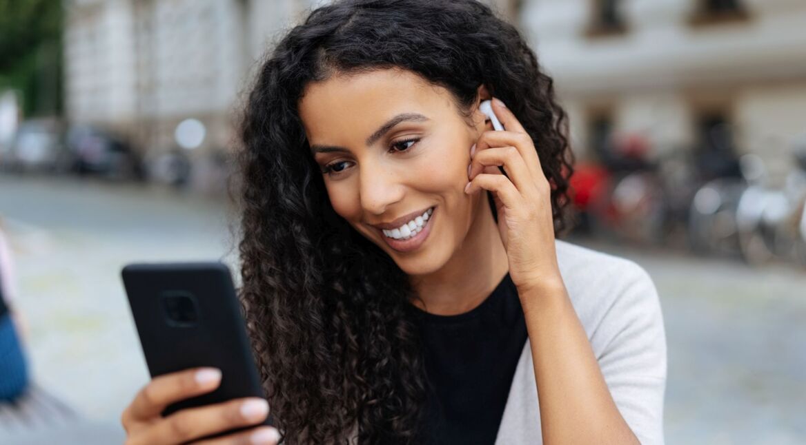 Frau hört mit Bluetooth-Kopfhörern Musik vom Smartphone