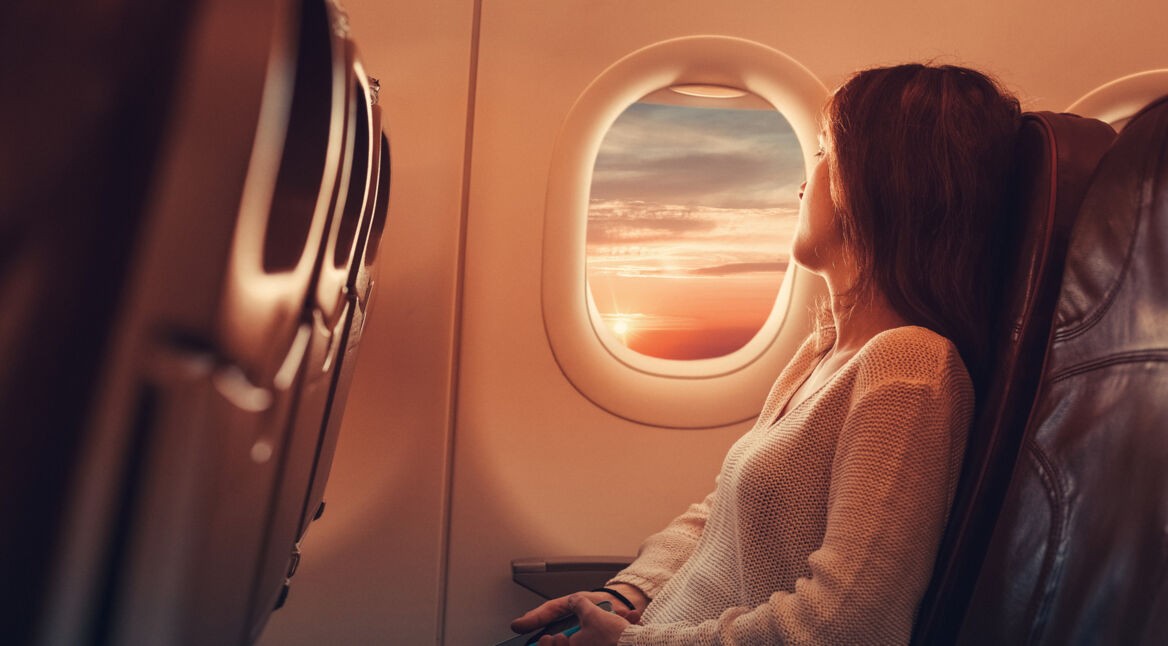 Eine Frau sitzt im Flugzeug und schaut entspannt aus dem Fenster
