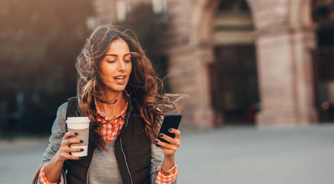 Eine Frau trinkt Kaffee und hat ein iPhone in der Hand