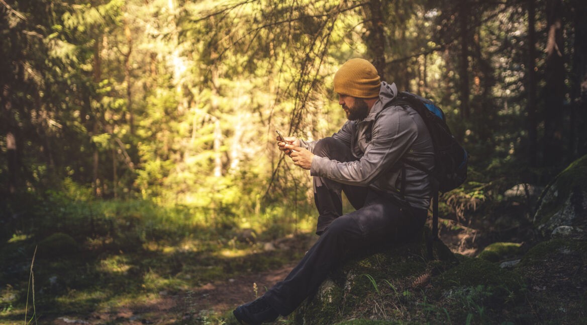 Ein Mann beim Wandern im Wald mit Smartphone