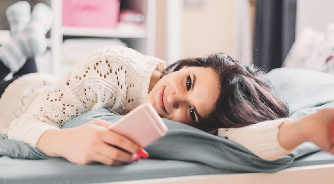 Frau liegt auf dem Bett und nutzt WhatsApp
