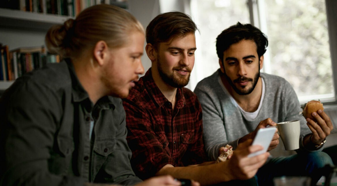 Drei junge Gamer chatten über das Smartphone mit ihrem Freunden.