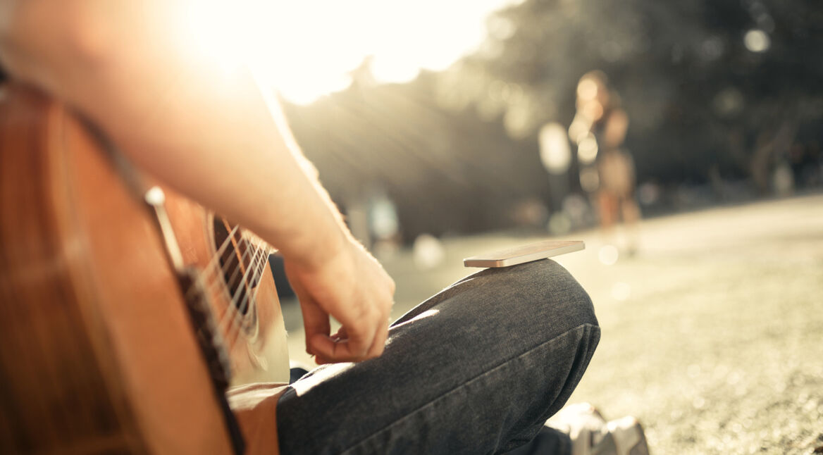 Ein Mann stimmt am See seine Gitarre via Smartphone