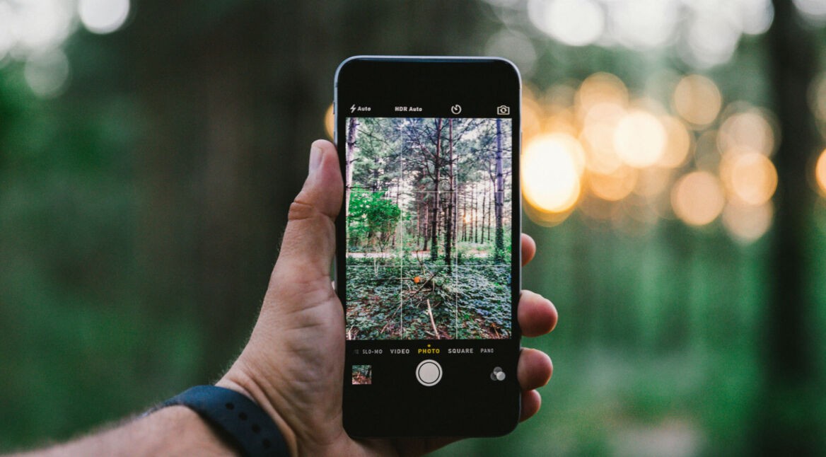 Junger Mann schießt mit seinem iPhone ein Foto vom Wald.
