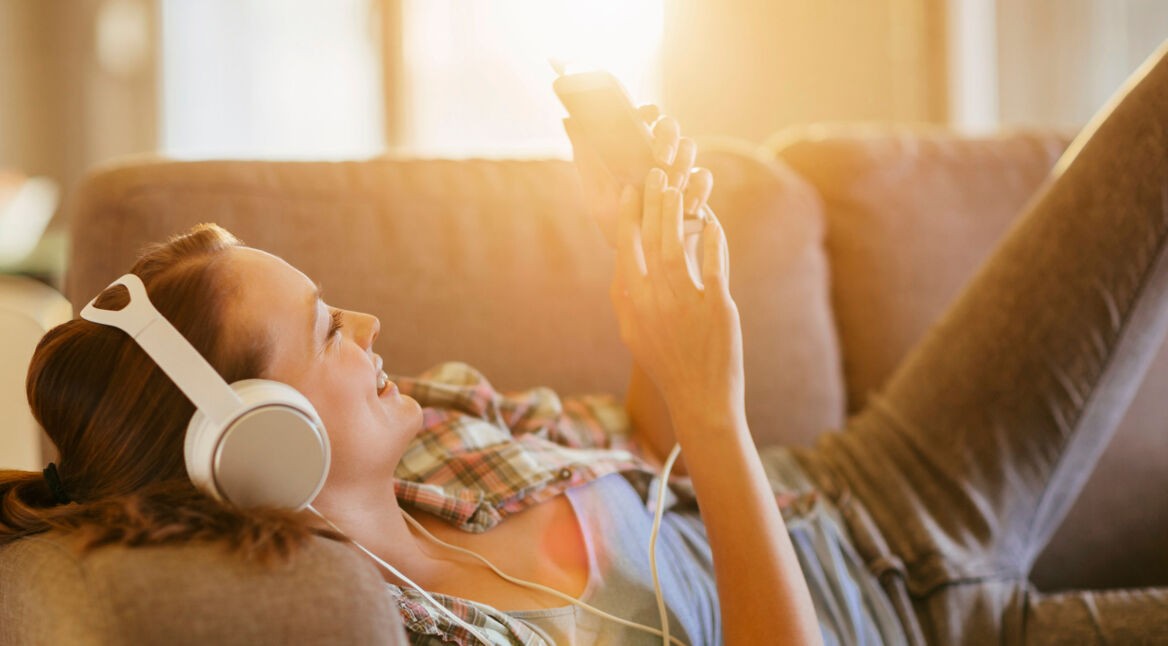 Junge Frau hört ein Hörbuch via Smartphone auf dem Sofa