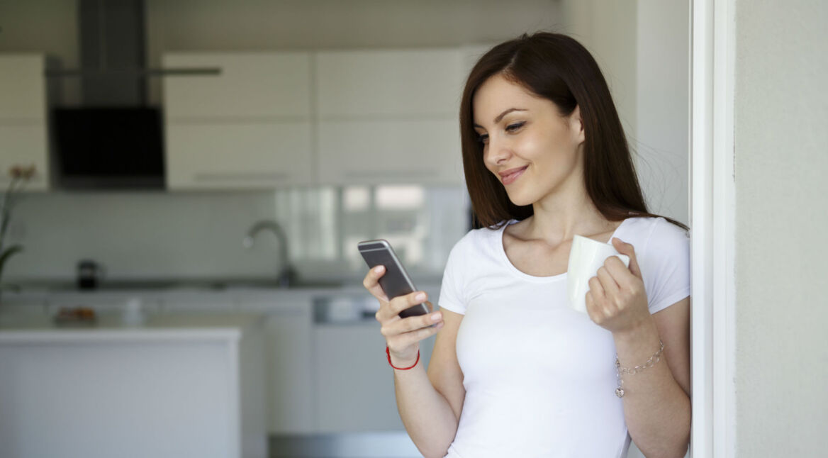 Junge Frau nutzt ihr Smartphone in der Küche.