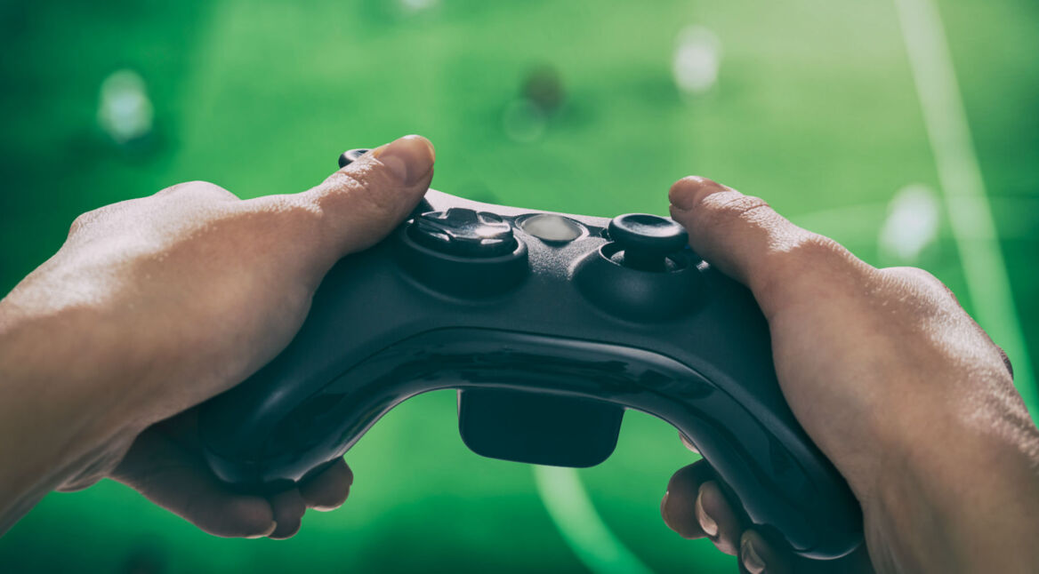 Zwei menschliche Hände halten einen Xbox-Controller und zocken ein Spiel am TV.