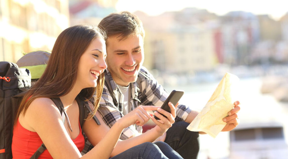 Junges Paar navigiert mithilfe von Smartphone und Stadtplan.