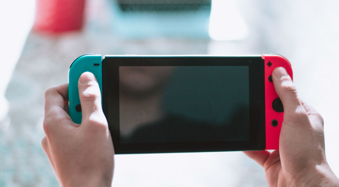 Nintendo Switch-Konsole mit bunten Joy-Con-Controllern liegt in menschlichen Händen.