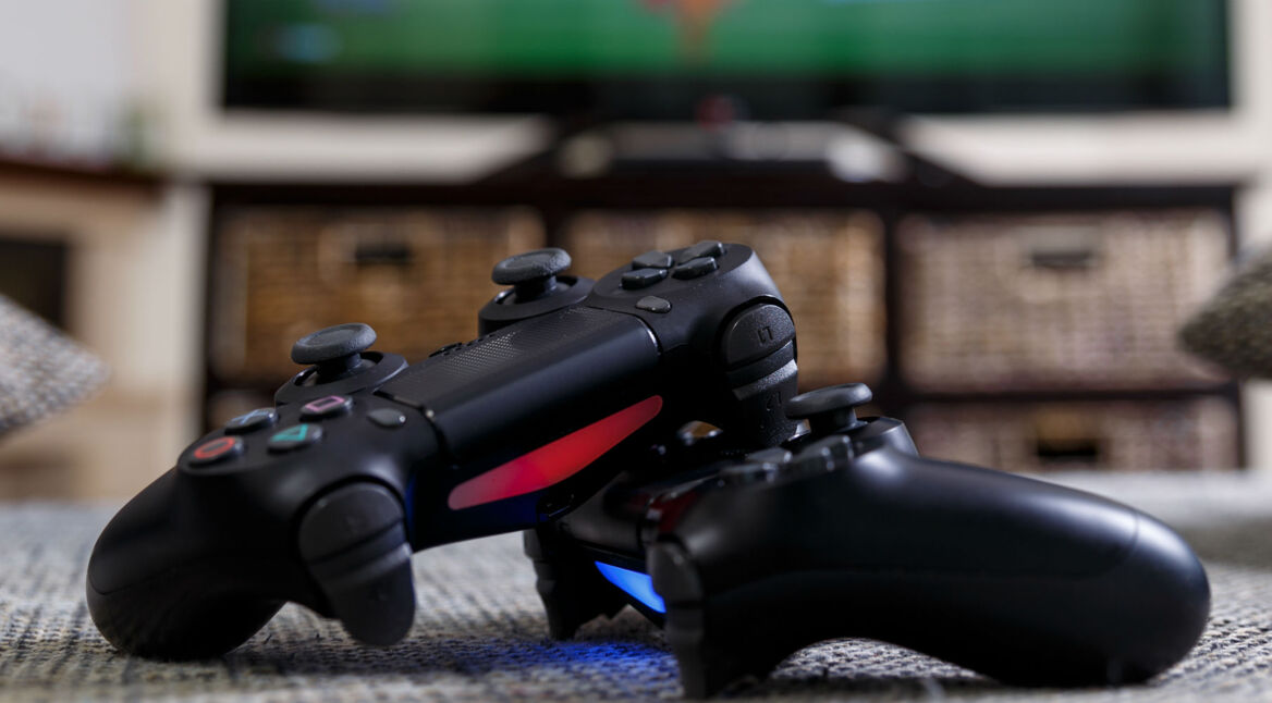 Zwei PS4-Controller liegen auf dem Teppich vor dem Fernseher.