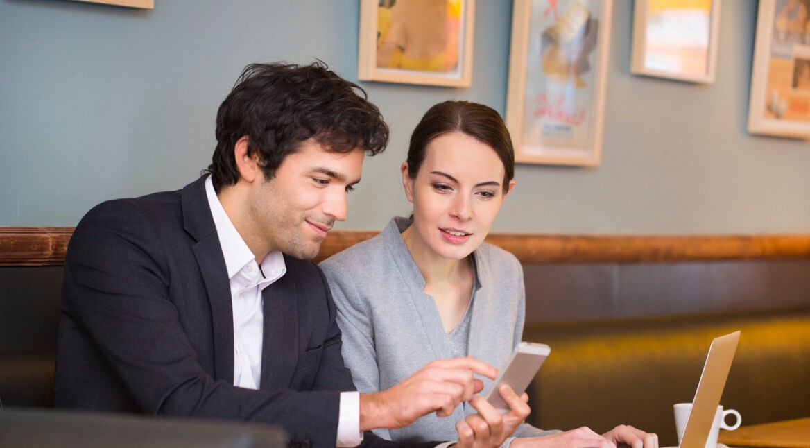 Ein Mann nutzt via Smartphone den Hotspot einer Frau auf dem Laptop