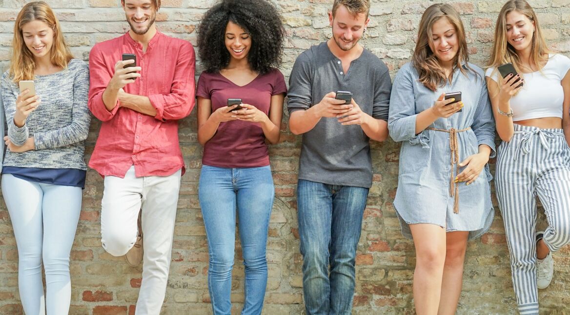 Junge Leute lehnen an einer Mauer und verfassen SMS-Nachrichten