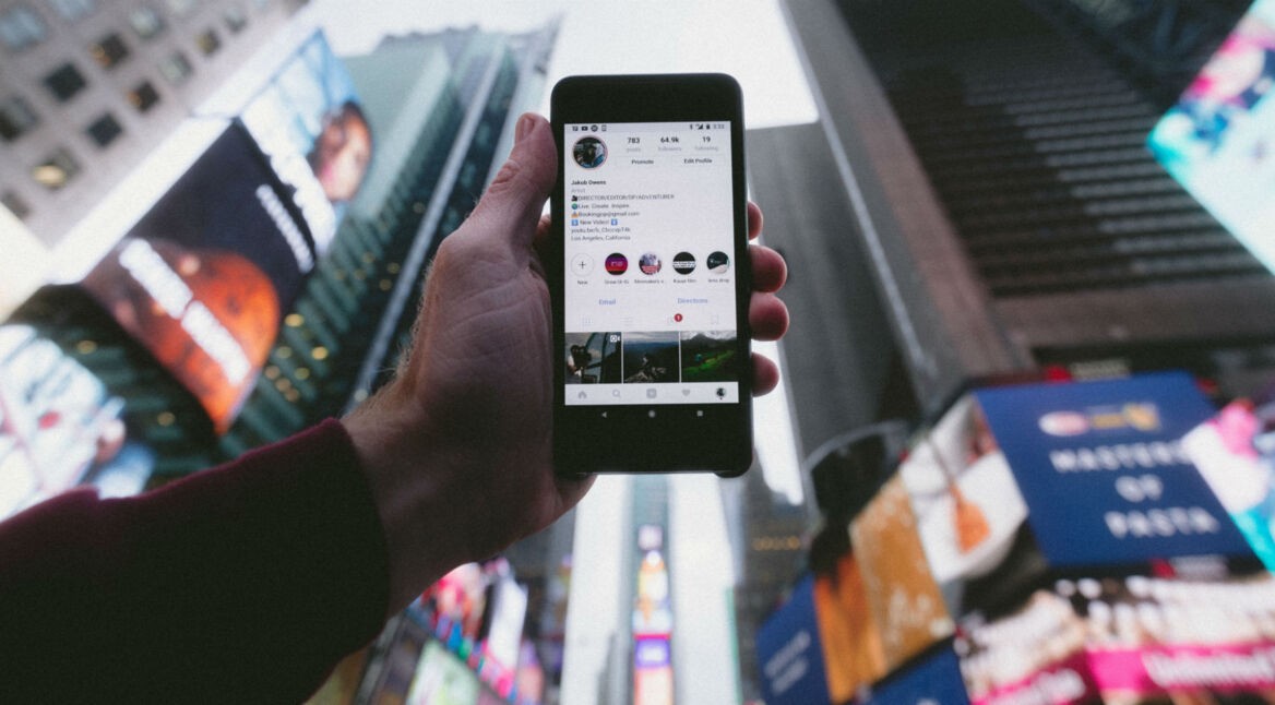 Instagram-Profil auf Smartphone, welches in die Luft gehalten wird.