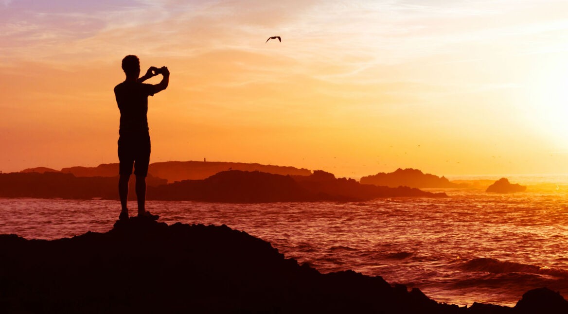 Junger Mann macht mit seinem Smartphone ein Foto vom Sonnenuntergang.