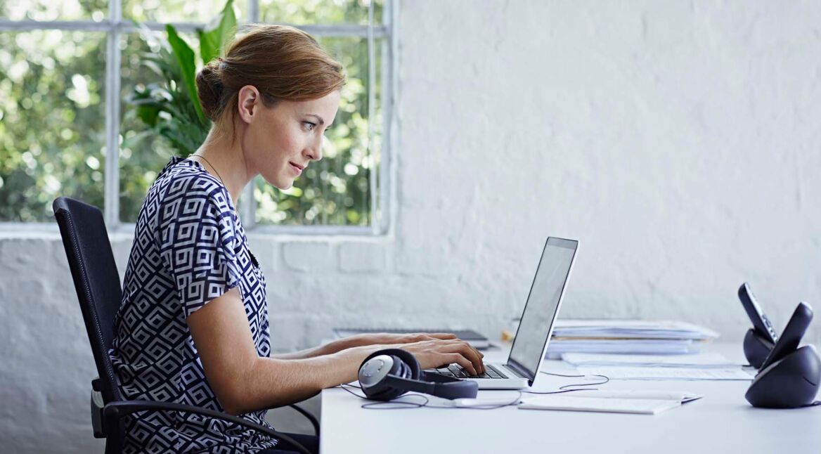 Junge Frau sitzt am Schreibtisch und arbeitet am Laptop