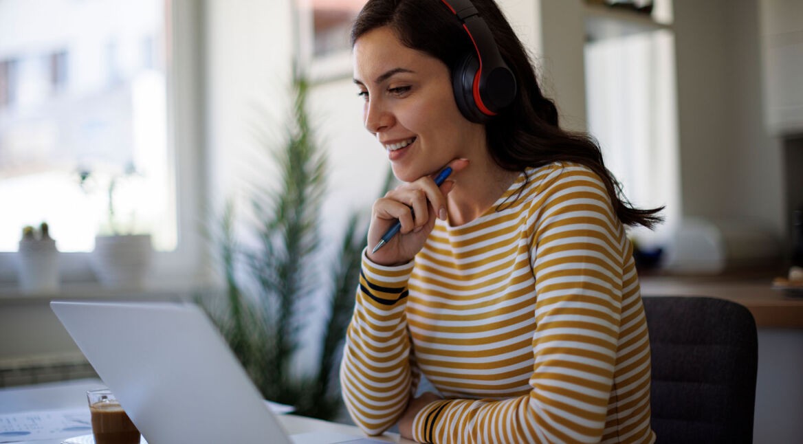 Eine junge Frau arbeitet an einem Laptop und nutzt ein kabelloses Headset